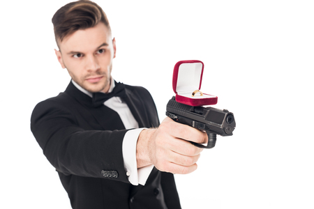 male killer in black suit aiming with gun with proposal ring, isolated on whiteの写真素材