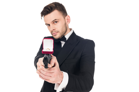 handsome secret agent in black suit aiming with handgun with proposal ring, isolated on whiteの写真素材