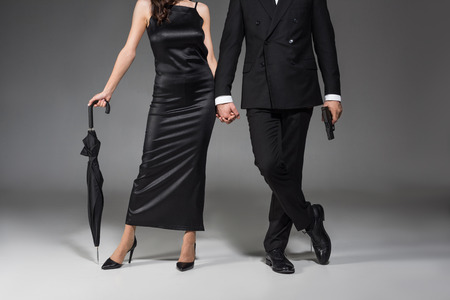 cropped view of couple of killers posing with handgun and umbrella on greyの写真素材