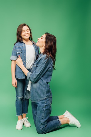 smiling mother embracing daughter with eyes closed on green background