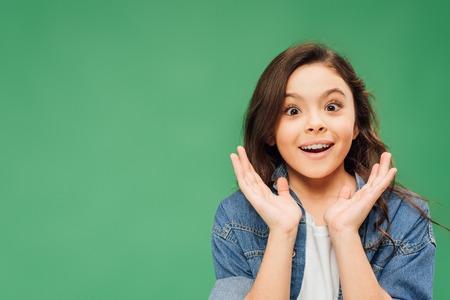 excited child gesturing with hands and looking at camera isolated on green