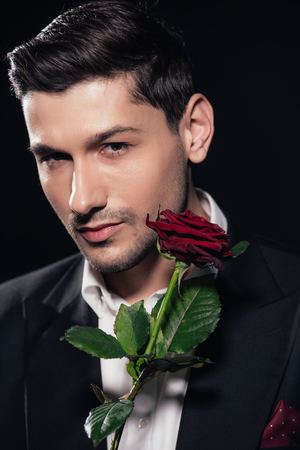portrait of handsome man in suit holding red rose isolated on blackの写真素材