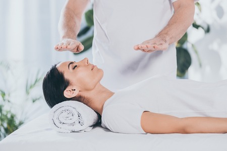 cropped shot of male healer doing reiki treatment session to young woman with closed eyesの写真素材
