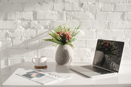 laptop with blank screen in white kitchen near business newspaperの写真素材