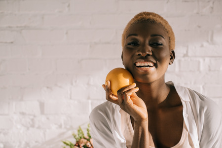 cheerful african american woman with short hair holding orangeの写真素材