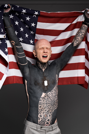 emotional tattooed man with closed eyes holding us flag isolated on greyの写真素材
