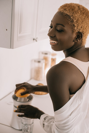 cheerful african american woman preparing squeezing orangeの写真素材