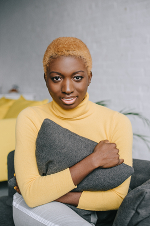 african american woman with short hair hugging grey pillowの写真素材