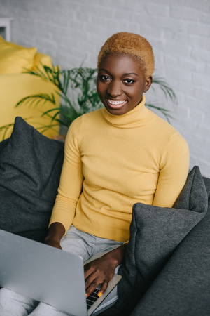 cheerful african american woman using laptop on sofaの写真素材
