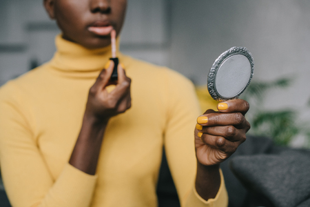selective focus of african american woman holding mirror and applying lip glossの写真素材