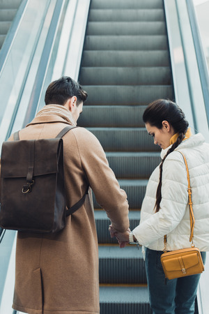 beautiful couple holding hands and going up on escalatorの写真素材