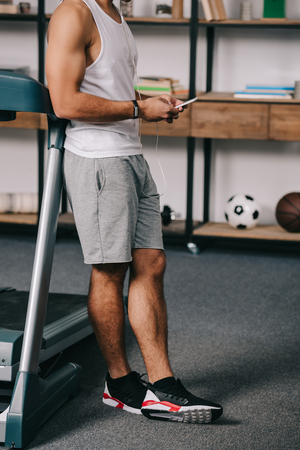 cropped view of man standing in sportswear and using smartphoneの写真素材