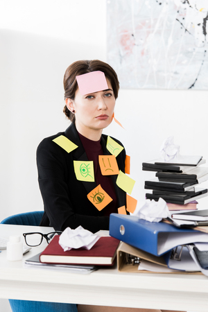 sad attractive businesswoman sitting with stickers on face and clothes in officeの写真素材