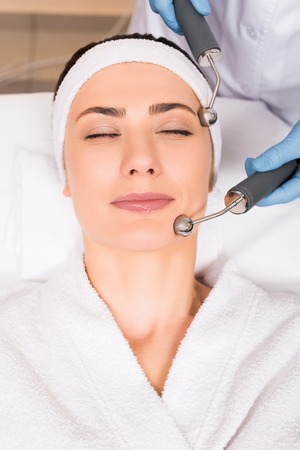 cosmetologist doing lifting massage on face with equipment to woman at beauty salonの写真素材