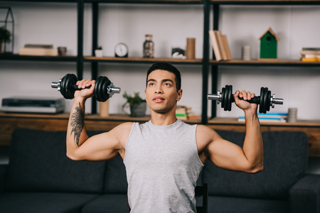 handsome mixed race athlete exercising with dumbbells in living roomの写真素材