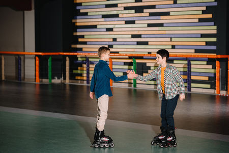 Pretty smiling children in roller skates stretching arms to each other
