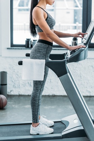 cropped shot of young sporty african american woman exercising on treadmill in gym