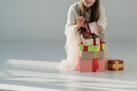 cropped image of woman in fashionable winter outfit squatting near gift boxes and opening present on whiteの写真素材