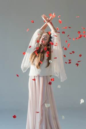 beautiful woman in stylish winter outfit standing under falling red roses petals isolated on whiteの写真素材