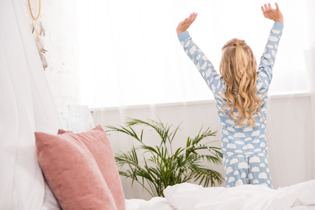 back view of kid in pajamas stretching near window in bedroomの写真素材