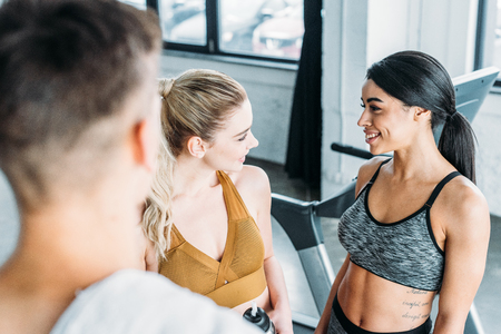 selective focus of young sportsman looking at cheerful sporty multiethnic girls smiling each other in gymの写真素材