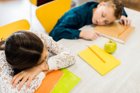high angle view of tired schoolkids in eyeglasses sleeping on table with books in library