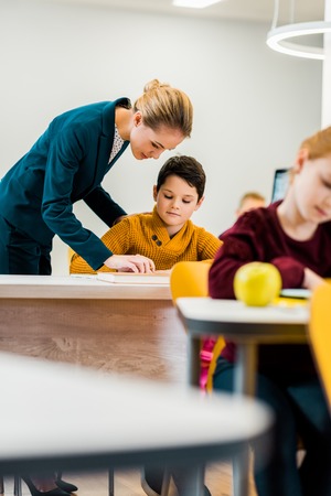 young female teacher helping schoolchildren studying at desksの写真素材