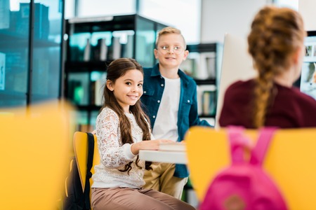 cute smiling schoolchildren studying with desktop computers in libraryの写真素材
