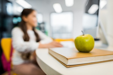 close-up view of apple on book and schoolchild sitting behind in libraryの写真素材