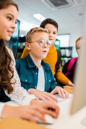 cropped shot of schoolchildren using desktop computer together in library