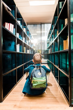 back view of schoolboy with backpack sitting on floor in libraryの写真素材