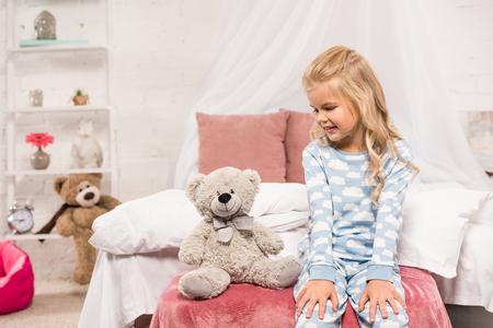 smiling cute kid sitting on bed with teddy bearの写真素材
