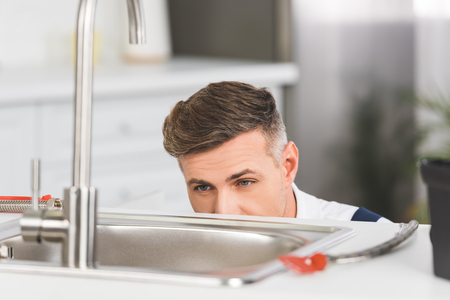 cropped view of adult repairman looking at sink at kitchenの写真素材