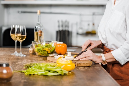 cropped image of mature woman cutting vegetables on wooden board in kitchenの写真素材