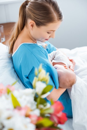 side view of smiling young mother breastfeeding newborn baby on bed in hospital roomの写真素材
