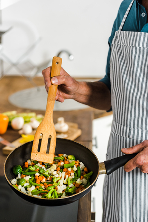 cropped image of middle aged man cooking vegetables on frying pan in kitchenの写真素材
