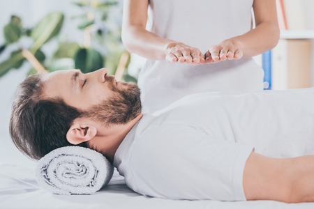 cropped shot of calm bearded man with closed eyes receiving reiki treatment on chestの写真素材