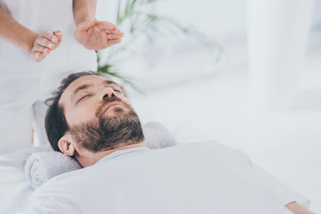 calm bearded man with closed eyes receiving reiki healing session above headの写真素材