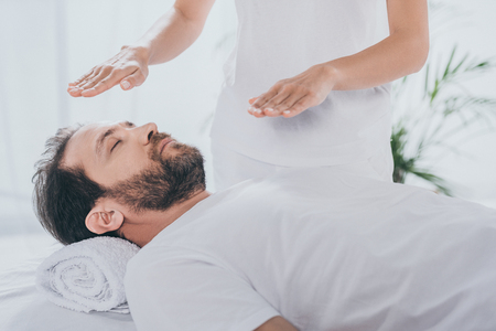 cropped shot of healer doing reiki healing session to calm bearded man with closed eyesの写真素材