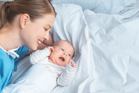 high angle view of happy young mother looking at adorable baby lying on bedの写真素材