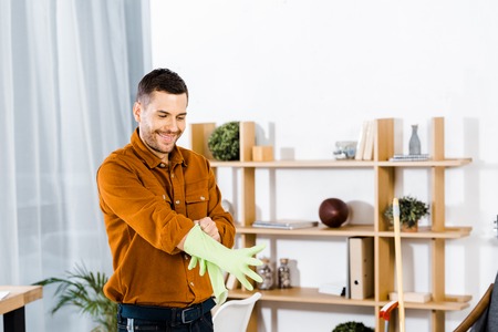 handsome man standing in modern living room and putting up rubber gloves
