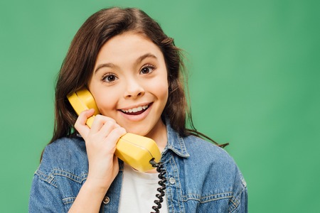 excited child talking on vintage telephone and looking at camera isolated on greenの写真素材