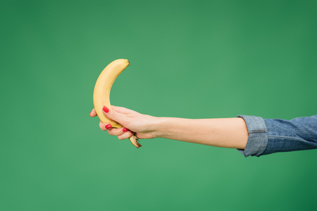 cropped view of woman holding banana in hand isolated on greenの写真素材