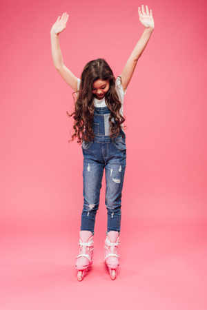 child in overalls rollerblading with outstretched hands on pink backgroundの写真素材