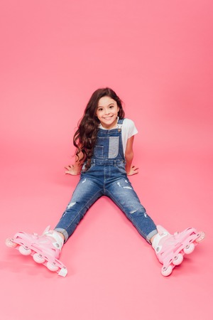 smiling child in overalls and roller blades looking at camera on pink backgroundの写真素材