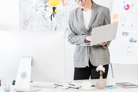 cropped image of smiling businesswoman holding laptop in officeの写真素材