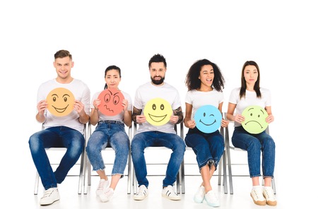 multicultural friends in blue jeans sitting on chairs and holding signs isolated on white
