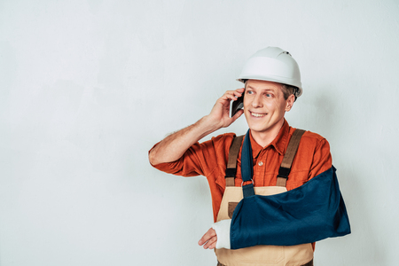 repairman with arm bandage talking on smartphone at white backgroundの写真素材