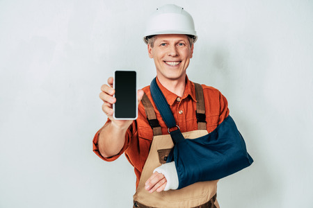 repairman with arm bandage showing smartphone at white backgroundの写真素材