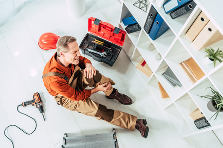 top view of repairman sitting on floor with injured knee in officeの写真素材